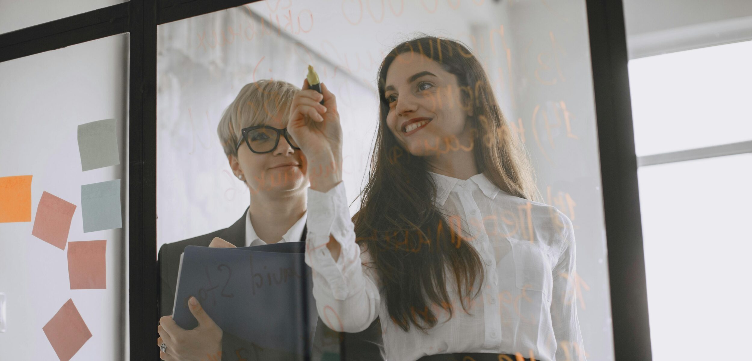 Two people planning with sticky notes on a wall.